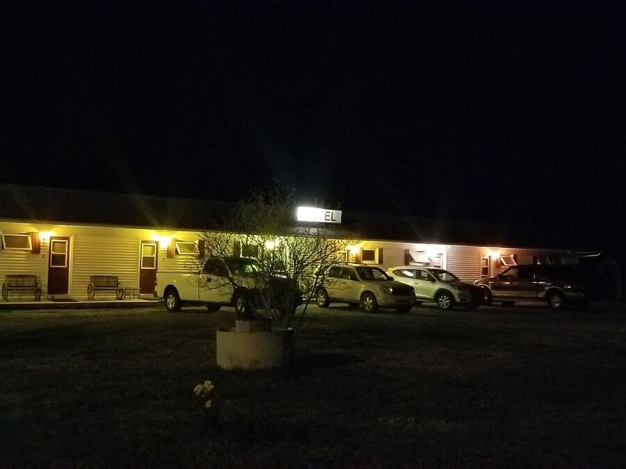 A motel with a sign reading "EL" at the entrance, a parking lot with several cars, and a small garden area with a planter.