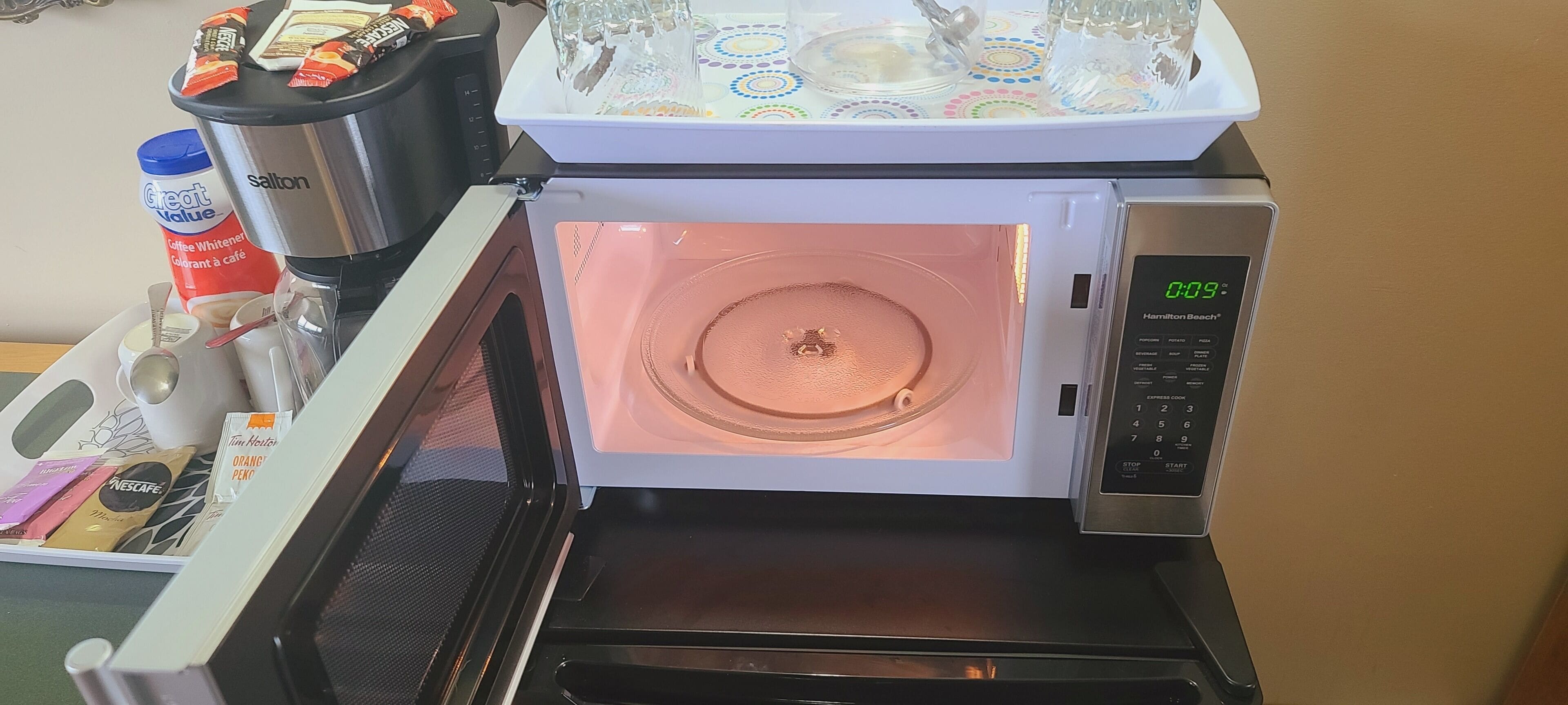 Un microondas con pantalla digital, una cafetera y una bandeja con cristalería.