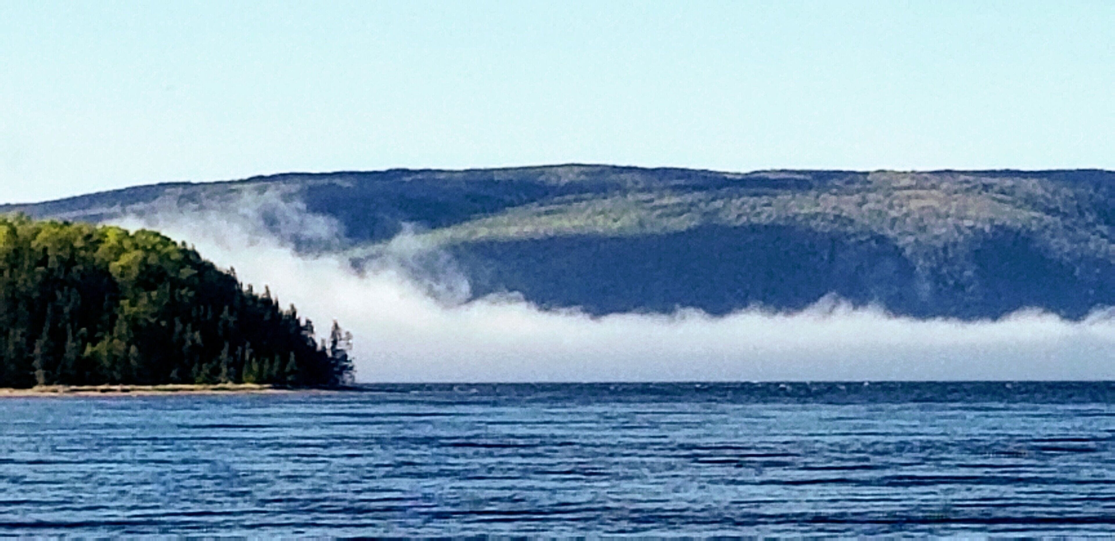 A coastal landscape with a forested island and a mountain in the background.