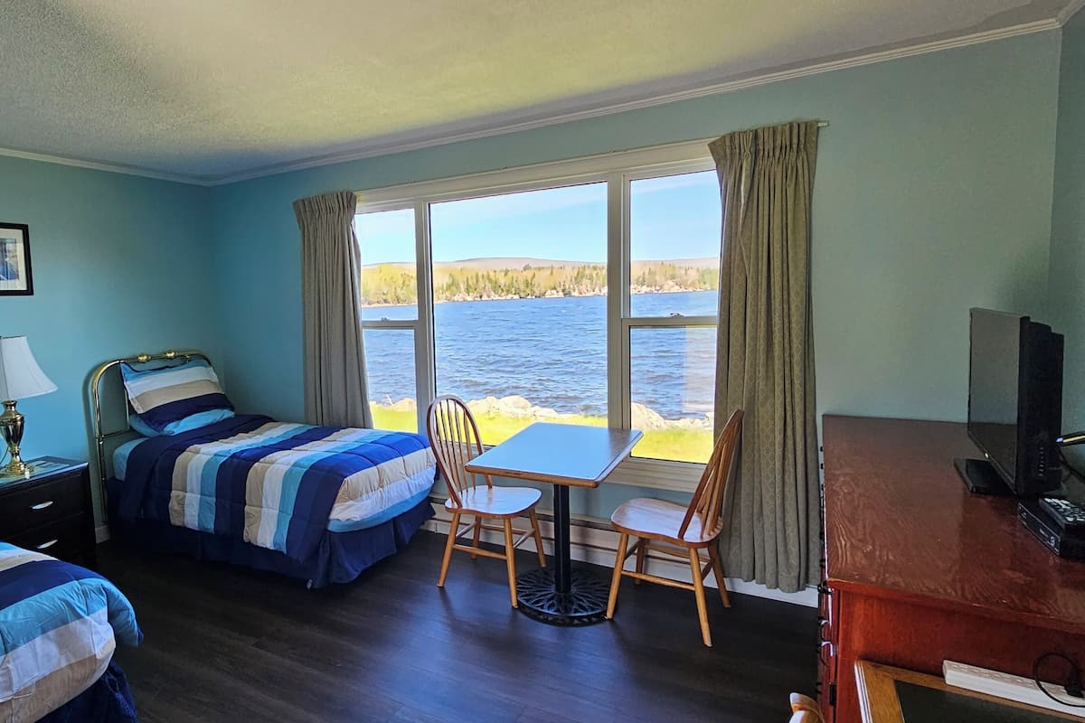 A hotel room with two beds, a desk, a chair, a TV, and a window with a view of a body of water.
