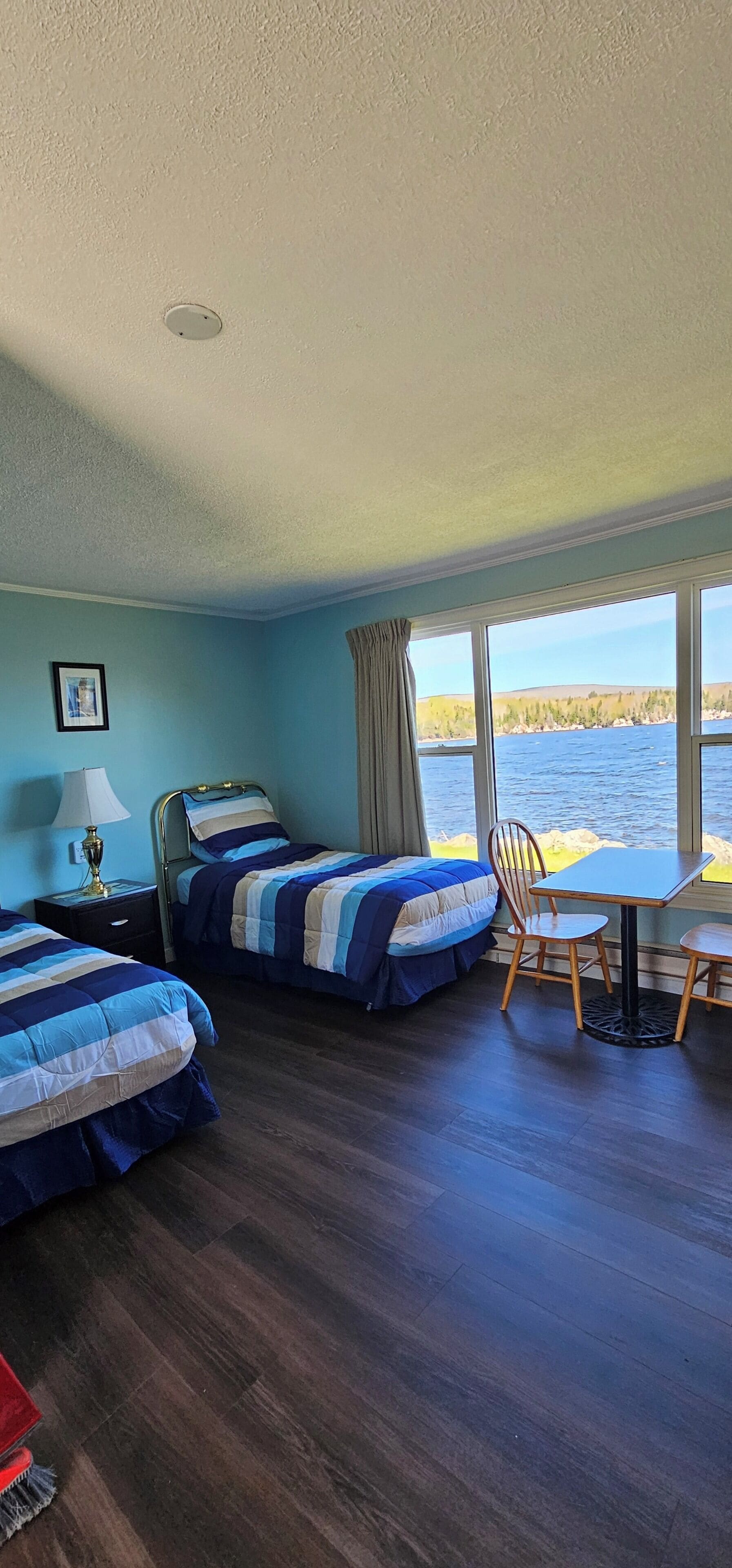 A room with two beds, a table, and a chair, with a view of a body of water.