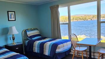 A room with two beds, a table, and a chair, with a view of a body of water.
