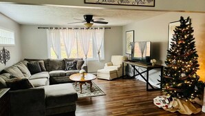 A cozy living room with a sectional sofa, a coffee table, a white armchair, a small table with a plant, a ceiling fan, a Christmas tree, and a sign above the sofa. - Peaceful Retreat near Ohiopyle and Fallingwater HOT TUB (Mill Run)