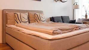 Ein ordentlich bezogenes Bett mit Kopfteil, zwei an der Wand befestigte Bilder und einem aufgehängten Hirschgeweih.