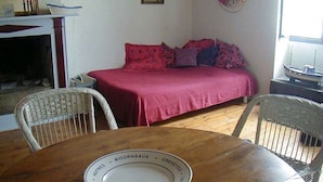 A cozy room with a wooden table, wicker chairs, a bed with red bedding, a blue lamp, and a life ring on the wall. - Typical house in Saint Sauveur (L'Île-d'Yeu)
