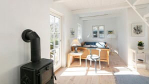 A cozy interior with a black wood stove, a wooden table with chairs, a sofa, and a small white table with a plant. - Stunning home in Allinge with WiFi (Allinge)