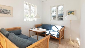 A room with a blue sofa, a round table, and two windows with white lamps. - Stunning home in Allinge with WiFi (Allinge)