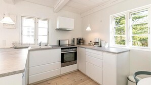A modern kitchen with white cabinetry, a built-in oven, a microwave, and a coffee maker. There are two windows providing natural light and a view of greenery outside. - Stunning home in Allinge with WiFi (Allinge)