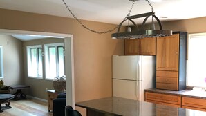 Een keuken met een centraal eiland, houten kastjes en een hangende lamp.