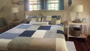 A bedroom with a large bed, two bedside tables, a window with curtains, and a wall-mounted lamp.