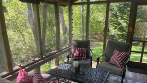 A covered outdoor seating area with a table and chairs, surrounded by a wooden deck and glass panels.