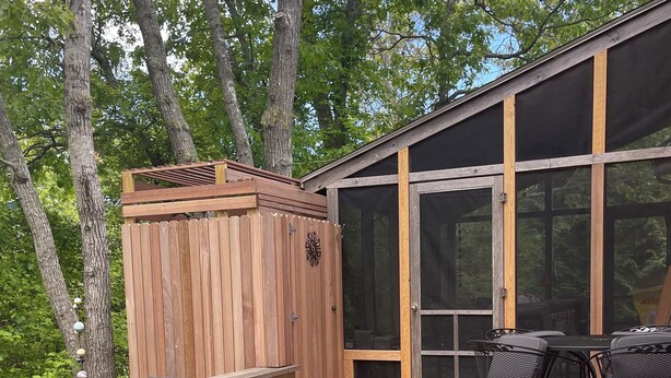 A wooden deck with a covered grill, a table with chairs, and a covered seating area.