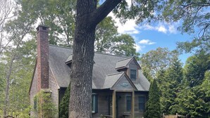 A house with a large tree in the front yard, a wooden fence, and a well-maintained lawn.
