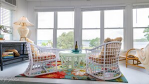 A room with a large window, a white ceiling fan, a small round table with a bottle and glasses, and two wicker chairs with cushions. - L👀K!! 3 KING BEDS - Private Boat Ramp - FREE NETFLIX - Lakefront Lake Powell!!! (Panama City Beach)