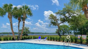 A swimming pool with two blue lounge chairs, surrounded by palm trees and a view of a lake. - L👀K!! 3 KING BEDS - Private Boat Ramp - FREE NETFLIX - Lakefront Lake Powell!!! (Panama City Beach)