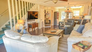 A spacious living room with a white leather sofa, a coffee table, and a fireplace. A staircase with a railing leads to an upper level. - L👀K!! 3 KING BEDS - Private Boat Ramp - FREE NETFLIX - Lakefront Lake Powell!!! (Panama City Beach)