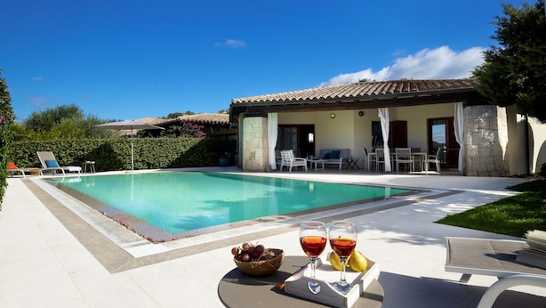 A poolside area with a table set for two, a basket of grapes, and two glasses of red wine. - VILLA IPPOCAMPO private pool and close to the sandy beach (Capo Coda Cavallo)