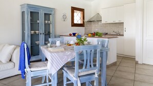 A dining area with a table set for two, a blue cabinet, and a kitchen in the background. - VILLA IPPOCAMPO private pool and close to the sandy beach (Capo Coda Cavallo)