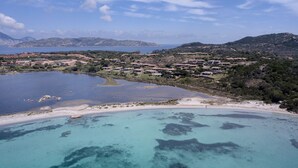 An aerial view of a coastal area with a beach, clear blue waters, and a residential area with houses. - VILLA IPPOCAMPO private pool and close to the sandy beach (Capo Coda Cavallo)