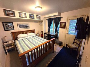 A bedroom with a bed, bedside table, chair, desk, and window with curtains.