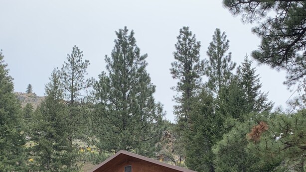 A rustic cabin with a wooden balcony, stone foundation, and two garage doors. - Log cabin in the bitterroot mountains (Sula)