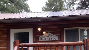 A cabin with a wooden deck, a metal roof, and a stone foundation. - Log cabin in the bitterroot mountains (Sula)