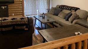 A cozy living room with a wooden ceiling, a ceiling fan, a television, a sofa with patterned cushions, and a coffee table. - Log cabin in the bitterroot mountains (Sula)
