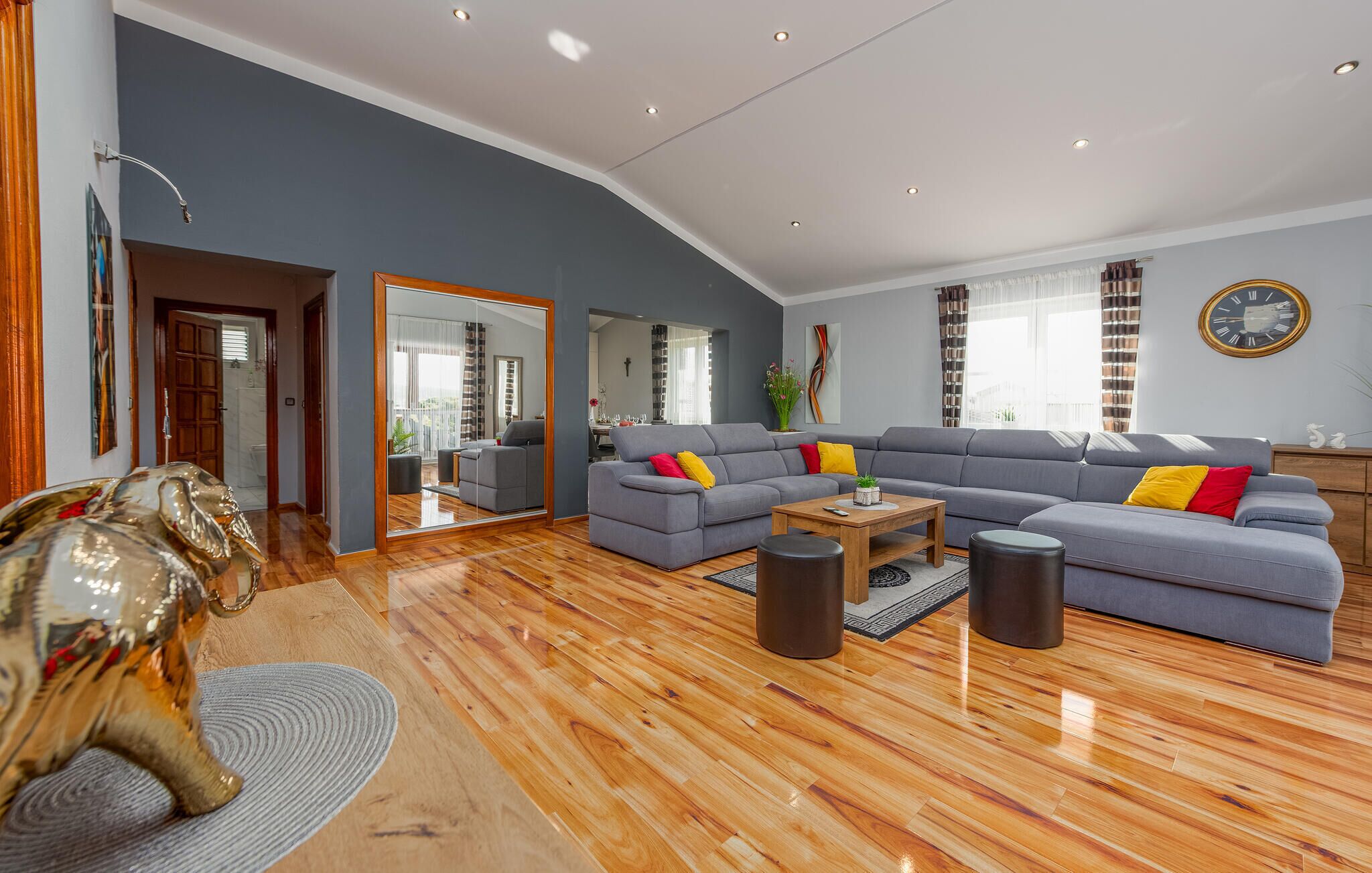 Uma sala de estar moderna com um sofá cinzento, piso de madeira e um espelho grande.