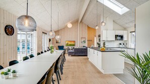 Cozinha moderna com armários brancos, sala de jantar com uma mesa comprida e cadeiras, e luminárias pendentes.