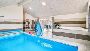 Piscina interna com um escorregador azul, uma banheira de hidromassagem e uma porta de vidro que dá para uma área externa.