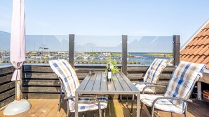 Een houten terras met tafel en stoelen, met uitzicht op een jachthaven met boten.
