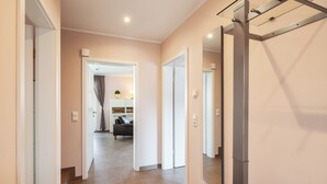 A modern hallway with a sliding door, a large mirror, and a glimpse of a living area with a sofa and a plant. - Villa Dalu am See - 5* luxury vacation home (Göhren-Lebbin (OT Untergöhren))
