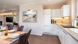 A modern kitchen with white cabinets, a stone backsplash, and a dining area with a table set for two. - Villa Dalu am See - 5* luxury vacation home (Göhren-Lebbin (OT Untergöhren))