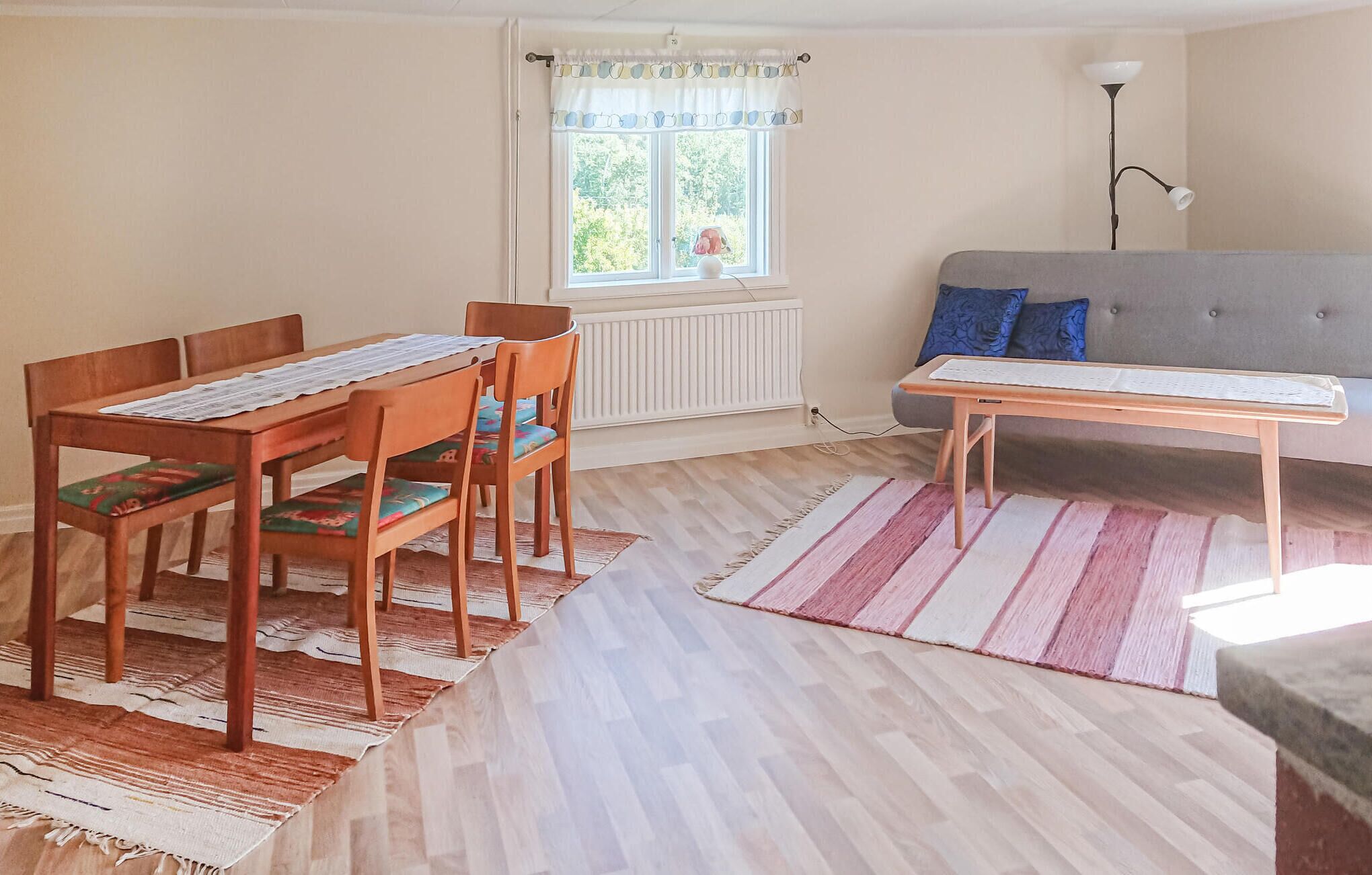 Een kamer met een eettafel en stoelen, een bank, een raam met gordijnen en een lamp.