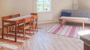A room with a dining table and chairs, a sofa, a window with curtains, and a lamp.