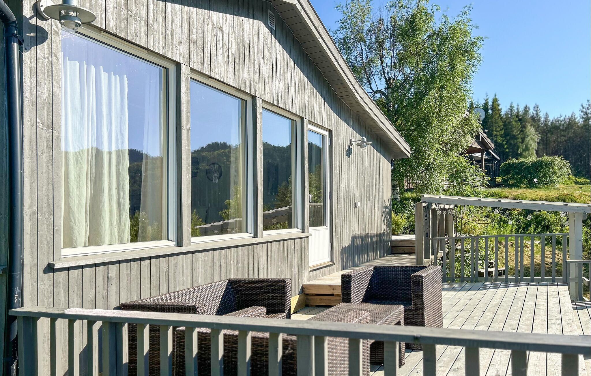 A wooden building with large windows, a deck with wicker furniture, and a view of trees and hills.