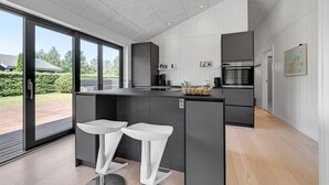 Una cocina moderna con una isla central, dos taburetes blancos de bar, un horno empotrado y un amplio ventanal con vistas al exterior.