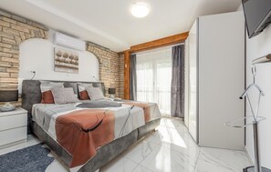 Una camera da letto moderna con parete in pietra, un letto con copriletto decorato, un comodino, un armadio e un'ampia finestra con tende.