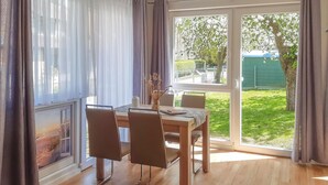 A dining area with a table and chairs, a vase with dried flowers, and a view of a green garden through a glass door. - 2 bedroom awesome home in Behrenhoff (Behrenhoff)
