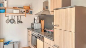 A compact kitchen with wooden cabinets, a microwave, a toaster, and a coffee maker. There are hanging utensils and a basket on the shelf. - 2 bedroom awesome home in Behrenhoff (Behrenhoff)
