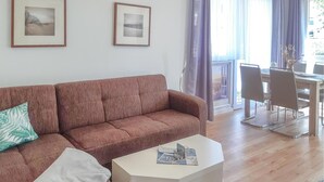 A living room with a brown sofa, a white side table, and a dining area with a table and chairs. - 2 bedroom awesome home in Behrenhoff (Behrenhoff)