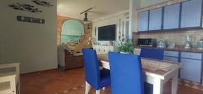 A dining area with a table, chairs, a television, and a kitchen with cabinets and appliances.