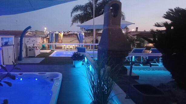 A pool area with a hot tub, lounge chairs, and umbrellas.