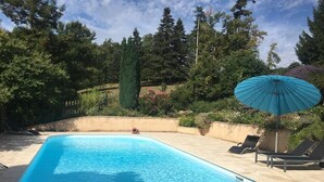 A swimming pool with a curved edge, surrounded by a concrete deck. There are lounge chairs and a blue umbrella. - Pretty stone house with swimming pool in magnificent agricultural area (Bonnes)