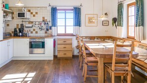 A kitchen with a wooden table and chairs, a built-in oven, and a window with curtains.