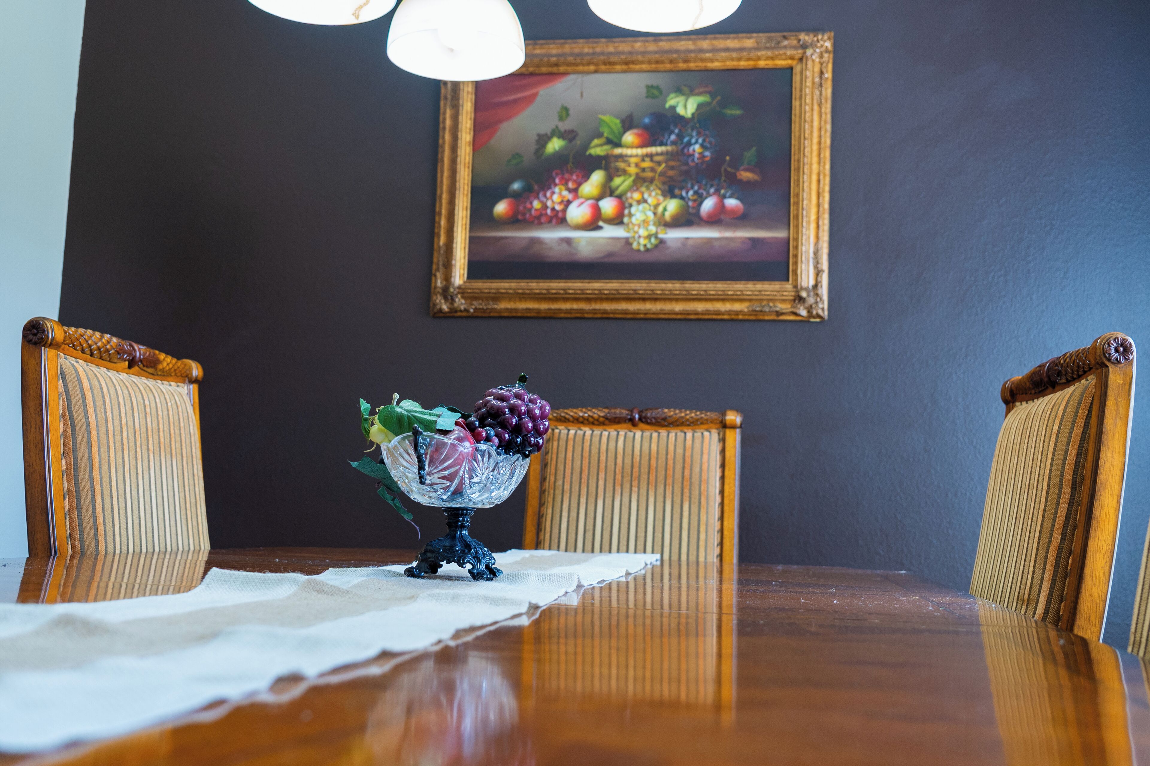 A dining table with a fruit bowl, two chairs, and a painting on the wall.