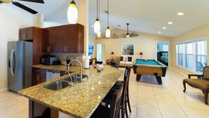 Eine geräumige Küche mit Granit Arbeitsplatten, einem eingebauten Backofen und einem Kühlschrank. Es gibt einen Billardtisch und eine gemütliche Sitzecke mit einer Couch und Sesseln.