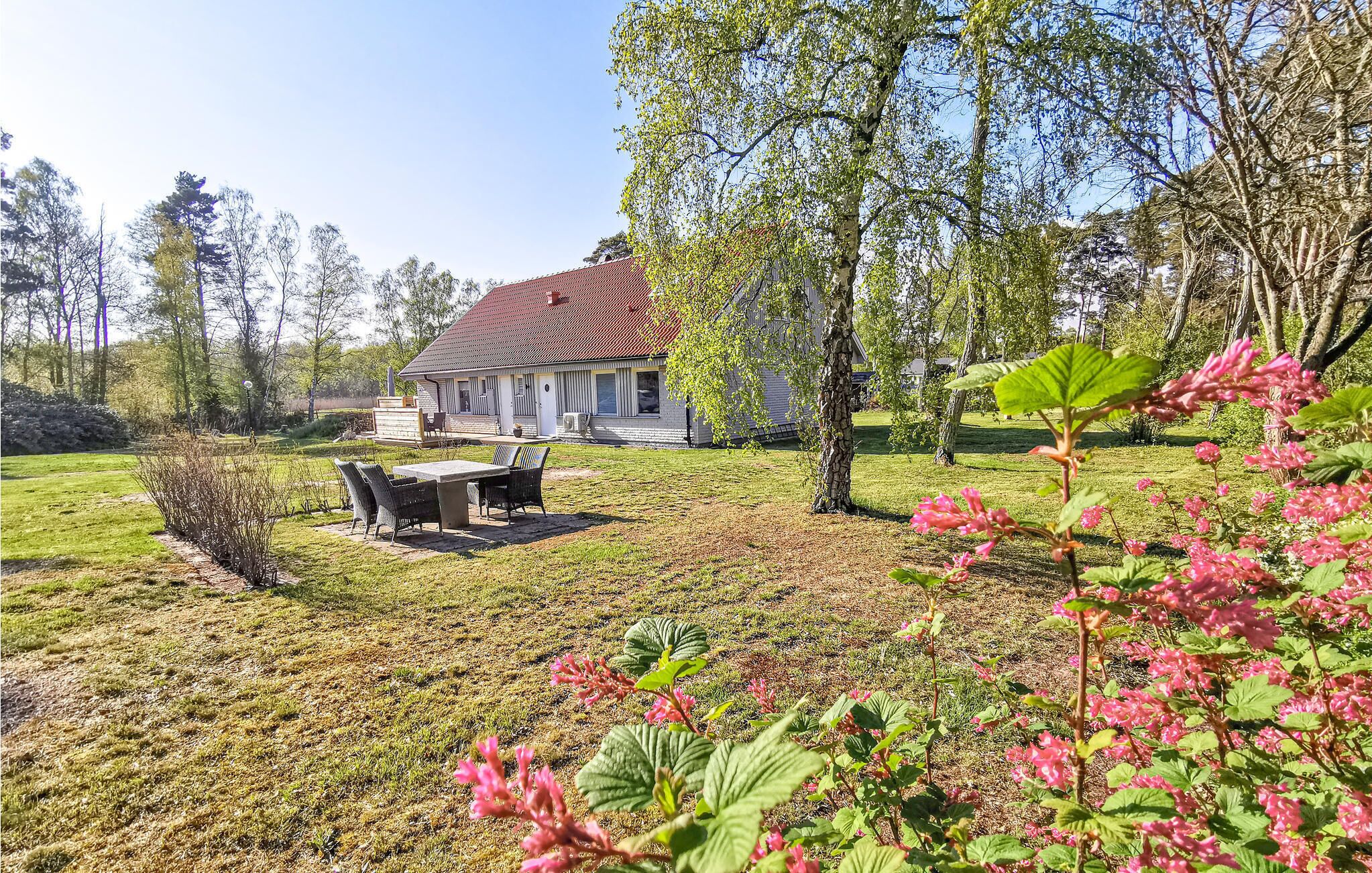 A house with a red roof, a patio with outdoor furniture, and a garden with pink flowers.