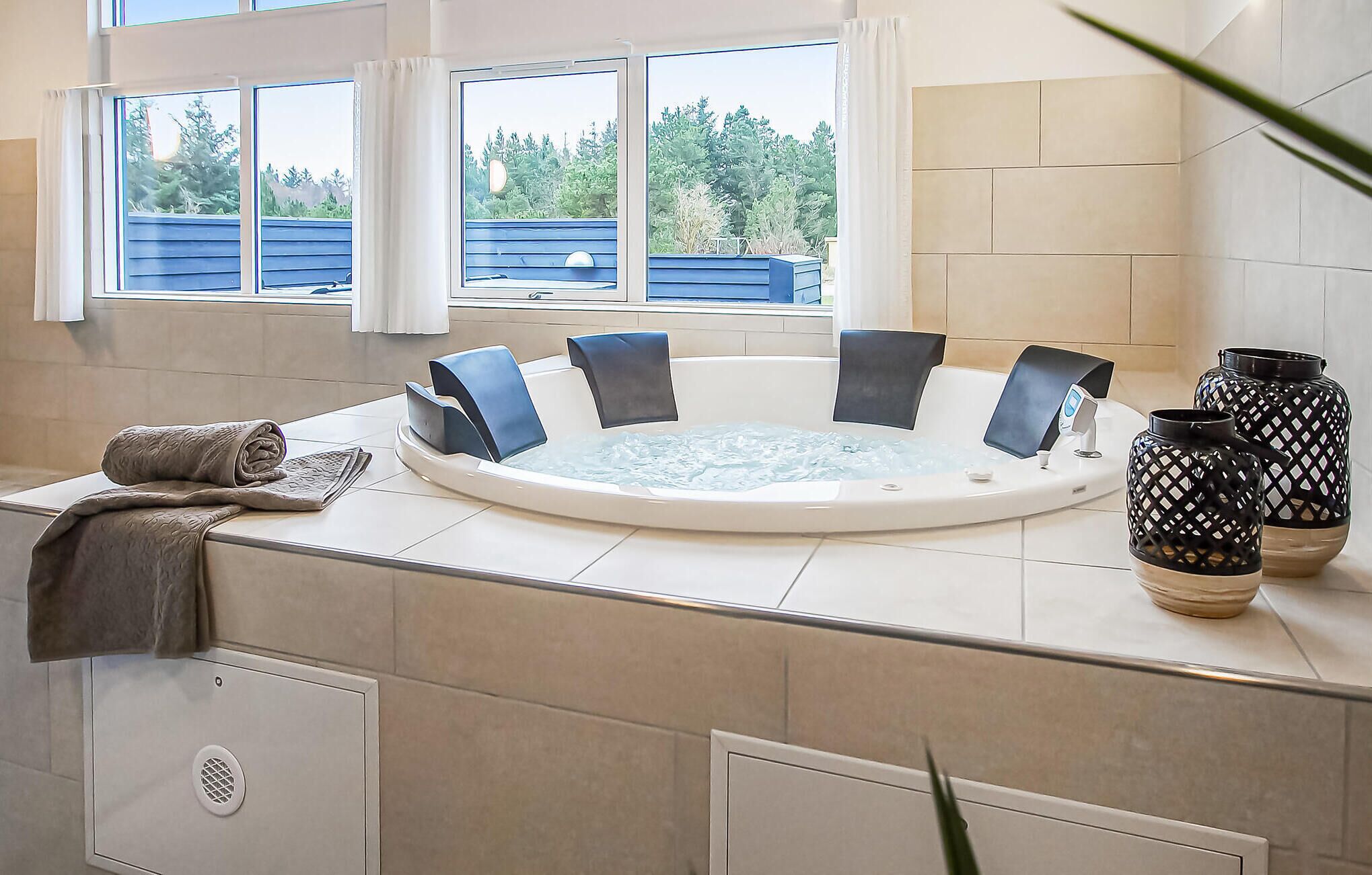 A modern bathroom with a freestanding bathtub, large windows, and decorative vases.