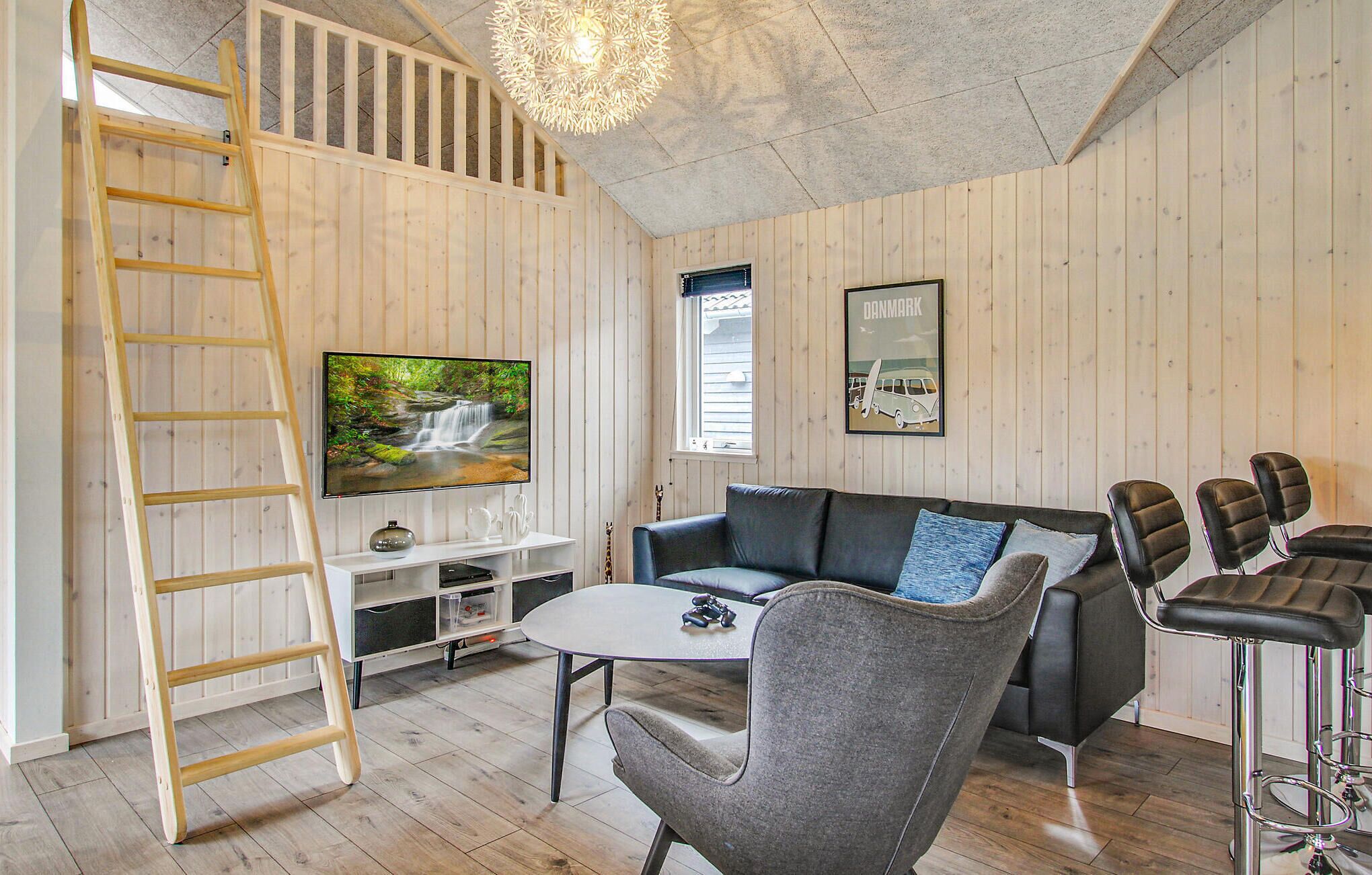 A wooden-paneled room with a TV, a sofa, a coffee table, a ladder, and a bar area.